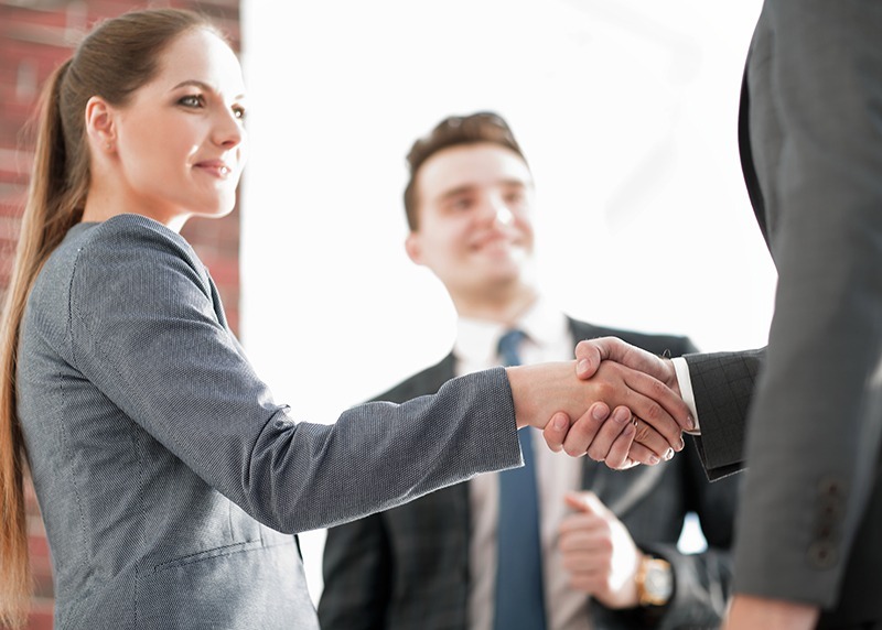 Woman shaking hands with another person while another man is looking at them