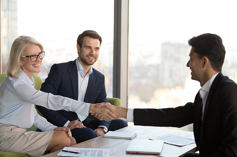 A woman shaking hands with a man while another man is looking at them