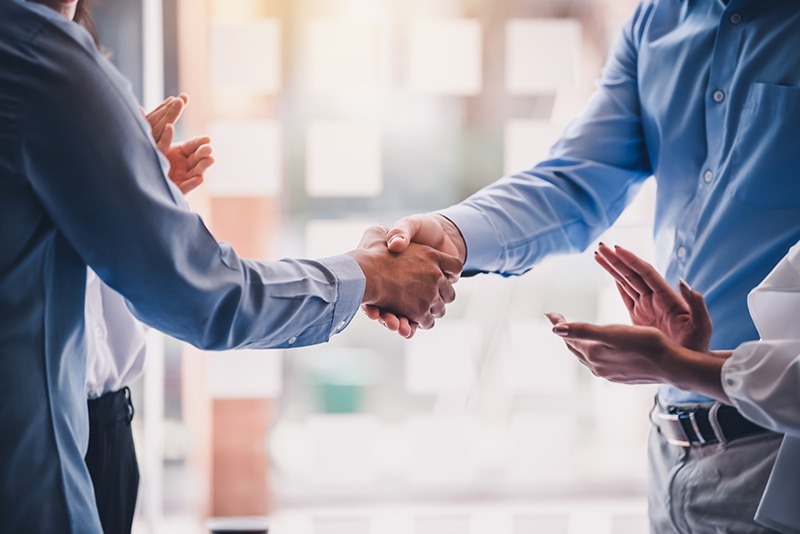 Two men shaking hands while a woman claps